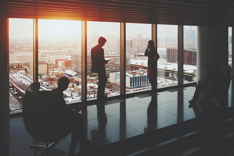 About Our Agency - Colleagues Making Calls in a High Rise at Sunset Against Large Plate Glass Windows